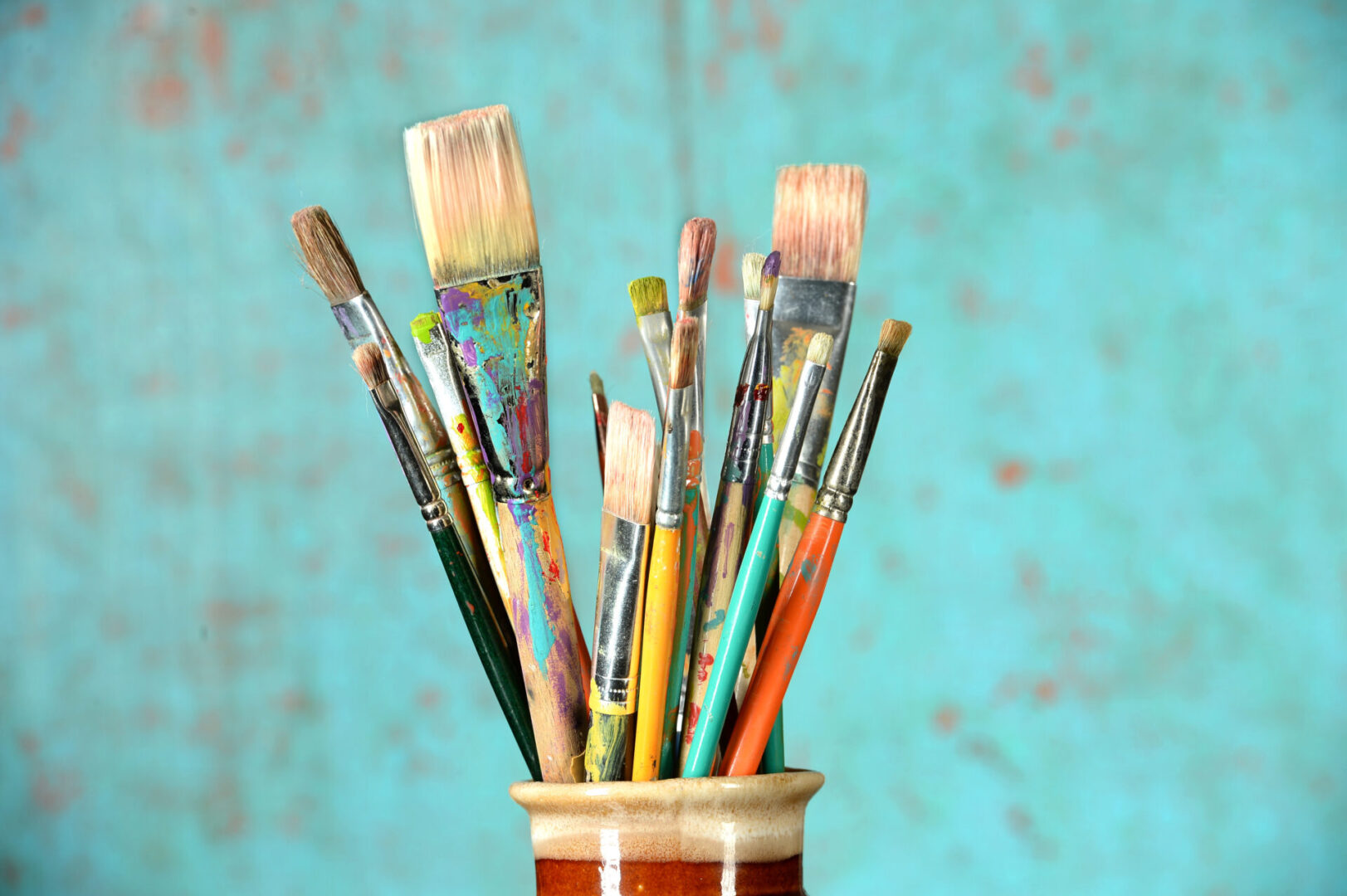 Artist paintbrushes in a jar over colorful background